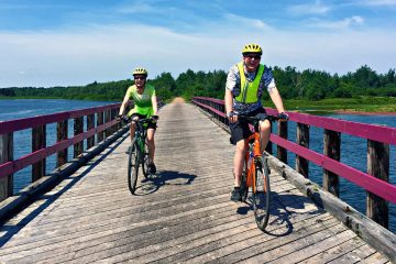 2 happy cyclists traversing a bridge along the traffic-free Confederation Trail, and bike paths of the National Park with our Confederation Trail Bike