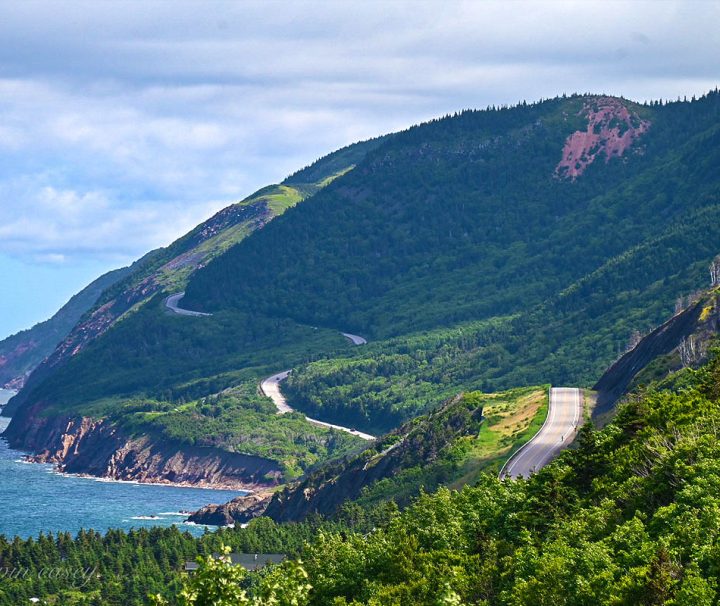 This image captures cyclists riding along the famous Cabot Trail in Cape Breton Highlands National Park, Nova Scotia