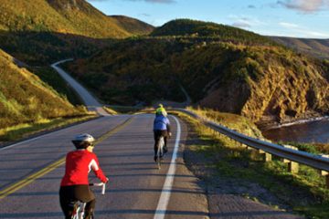This image captures cyclists riding along the famous Cabot Trail in Cape Breton Highlands National Park, Nova Scotia