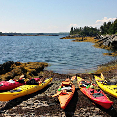 This image shows several colorful kayaks resting on a rocky shoreline in Nova Scotia, a popular activity in the area