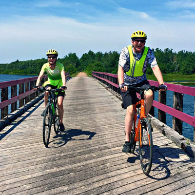 This image depicts a sunny day of cycling along the Confederation Trail in Prince Edward Island, likely near St. Peter's Bay, a popular route for tourists exploring the province by bicycle
