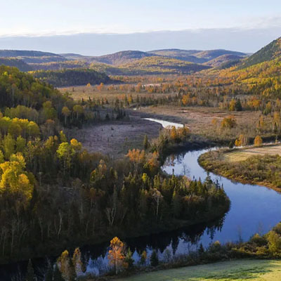 This image depicts a scenic river meandering through a forested valley during autumn