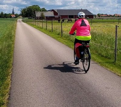 This image shows a person cycling on a paved rural path through the flat landscape of the Kattegattleden cycling route