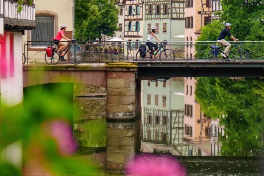 This scene depicts cyclists crossing a bridge in the Petite France district of Strasbourg, France