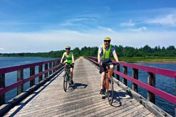 This image depicts a sunny day of cycling along the Confederation Trail in Prince Edward Island, likely near St. Peter's Bay, a popular route for tourists exploring the province by bicycle