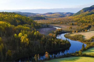 This image depicts a scenic river meandering through a forested valley during autumn