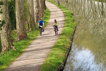 This image depicts a scenic moment in time featuring cyclists riding along a towpath beside the Canal du Midi in France