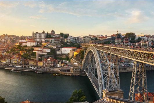 This image depicts a sunset view of the Dom Luís I Bridge in Porto, Portugal, a famous double-deck metal arch bridge spanning the Douro River