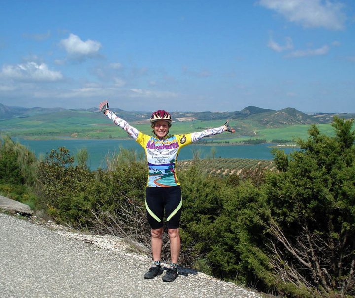 This image depicts a cyclist celebrating at a viewpoint during a scenic Andalusian bike tour in southern Spain