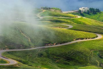 A scenic, winding mountain road known as a hairpin turn or switchback route, often found in hilly landscapes in the Pyrenees foothills